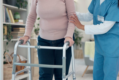 Caregiver, hands or elderly woman walking with walker for support